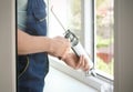 Construction worker sealing window with caulk