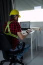 Construction Worker is sitting at his desk at the computer, looking at building plans, counting and thinking