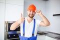 The construction worker, is straightening helmet on head, smiling and showing thumbs gesture up. Royalty Free Stock Photo