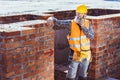 Construction worker in reflective vest and hardhat leaning on unfinished wall and talking