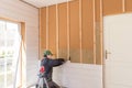 The worker makes finishing works of walls with a white wooden board, using laser line level. Building heat-insulating Royalty Free Stock Photo