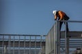 Construction worker on top of steel framing in white hard hat and orange long sleeve shirt