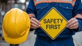 A construction worker holding a safety first sign with a yellow hardhat on the left side of the frame Royalty Free Stock Photo