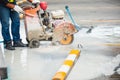A construction worker is using a concrete saw to cut through a wet concrete surface. Workers wear protective gloves and boots. A Royalty Free Stock Photo