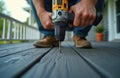 Construction worker using cordless drill installs composite decking boards for house renovation patio building. Carpenter screw Royalty Free Stock Photo
