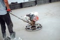 Construction worker using helicopter power tool and polishing sand and cement screed floor on the roof terrace of construction