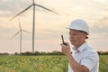 Construction worker with walkie-talkie against wind turbine farm. A man in white helmet holding a walkie talkie to check wind