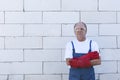 Construction worker wearing prfessional overalls and red protective gloves, standing near the white bricks wall