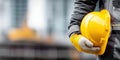 Construction worker holding a yellow hard hat in his gloved hand on a blurred background Royalty Free Stock Photo