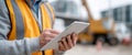 Construction worker wearing safety vest using digital tablet on site with blurred heavy machinery in background Royalty Free Stock Photo