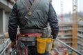 construction worker wearing tool belt and gloves stands on building site, showcasing various tools in yellow pouch. environment is Royalty Free Stock Photo