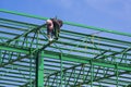 Construction worker is welding metal on green roof warehouse structure against blue sky