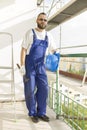 Construction worker in a work attire, protective gloves holds a helmet and a hammer. Work at high altitude. Scaffolding in the b Royalty Free Stock Photo