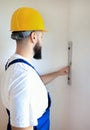 Construction worker is working on renovation of apartment. Builder is measuring and checking wall room using spirit level tool. Royalty Free Stock Photo