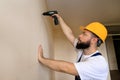 Construction worker works on renovation of apartment. Builder using electric screwdriver and screwing screw out of wall. Royalty Free Stock Photo