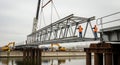 Construction Workers Erecting Steel Bridge Section Using Crane on Cloudy Day with Heavy Machinery and Water Royalty Free Stock Photo