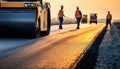 Construction workers and heavy machinery working on a new asphalt road at sunset, creating a smooth roadway. Royalty Free Stock Photo