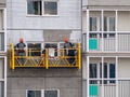 Construction workers installers high-rise workers industrial climbers, painters on the lift paint the facade of the building, comp Royalty Free Stock Photo