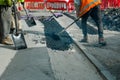 Construction workers placing hot tarmac after installation of new underground services, kerbs