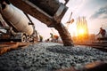 Construction workers pour concrete at a building site during sunset with cranes and steel reinforcement in the Royalty Free Stock Photo