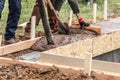 Construction Workers Pouring And Leveling Wet Cement Into Wood Framing