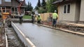 Construction workers in safety gear pour and level concrete for a house foundation, demonstrating teamwork and precision Royalty Free Stock Photo