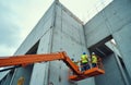 Construction workers in safety vests and helmets operate telescopic boom lift platform. They work high on massive concrete Royalty Free Stock Photo