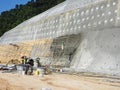 Construction workers are spraying liquid concrete onto the slope surface to form a retaining wall layer.