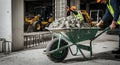 Construction Workers Transporting Concrete in Wheelbarrow on Building Site with Machinery and Protective Gear Under Bright Royalty Free Stock Photo