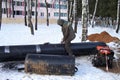 Construction works, the worker does cleaning of a big metal pipe by the electric tool for repair of a heating main, winter,