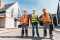 Constructors in helmets standing with coworker near houses