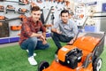 A consultant in a garden tools store shows a guy and a girl a lawn mower. Royalty Free Stock Photo