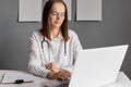 Consultation online. Research insurance. Beautiful young woman doctor wearing lab coat sitting in front of portable computer Royalty Free Stock Photo