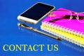 Contact us-business contacts. A written message on the background of a smartphone, a Notepad, glasses and a pen for writing. For
