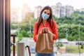 Contactless delivery of goods during Covid 19, coronavirus pandemic. The food delivery courier is holding a large paper bag in her