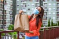 Contactless delivery of goods during Covid 19, coronavirus pandemic. The food delivery courier is holding a large paper bag in her