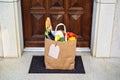 Contactless food delivery service concept. Paper bag with groceries delivered and left outside at entrance door. Online shopping.