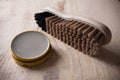 Container of shoe polish and brush on wooden background