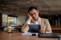 A contemplative Asian businessman looks pensive while holding a tablet, facing a problem at work