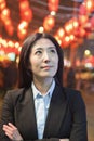 Contemplative Businesswoman standing on the street, red lanterns in the background