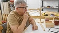 A contemplative grey-haired man sketches a design in his carpentry workshop surrounded by wooden tools and projects Royalty Free Stock Photo