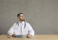 Contemplative satisfied doctor sitting at desk holding clipboard studio shot Royalty Free Stock Photo