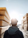 Contemplative worker facing stacks of lumber under a bright sky. Represents industry, construction, supply chain, or new Royalty Free Stock Photo