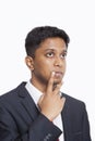 Contemplative young Asian businessman with hand on chin against white background