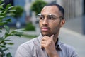Contemplative young man with glasses looking away thoughtfully in an urban setting, embodying introspection Royalty Free Stock Photo