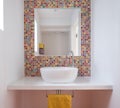 Contemporary bathroom with wash basin, colorful glass mosaic tiles, painted MDF shelf and mirror inset into the tiles. Royalty Free Stock Photo