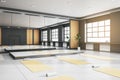 Contemporary group class in gym interior with yoga mats, wooden flooring, mirror with reflections, window with city view and