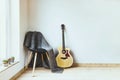 Contemporary home interior. Black chair covered with woolen gray blanket and acoustic guitar in front of an empty white wall. Royalty Free Stock Photo