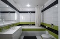 Contemporary interior of bathroom in modern flat. Black and green tile. Sink and mirror. Bath with shower.