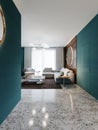 Contemporary living room studio, aquamarine walls with wooden panels and a round mirror, a white corner sofa and a black cabinet